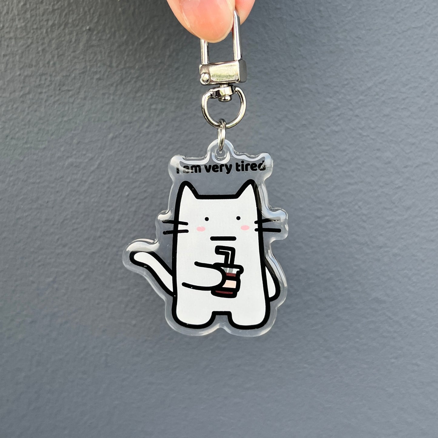 waterproof cat acrylic keychain with the text “I am very tired" on a plain background