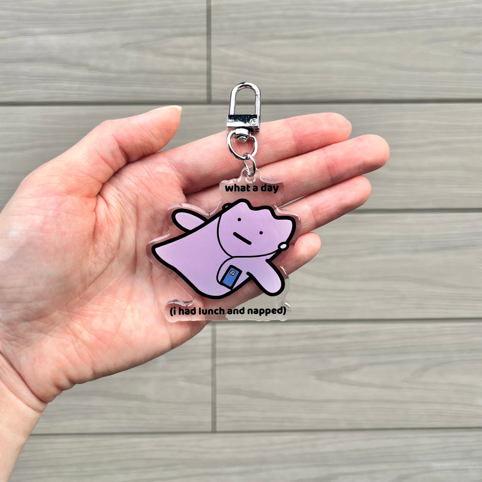 waterproof acrylic keychain with the text “What a day (I had lunch and napped)" on a person's hand
