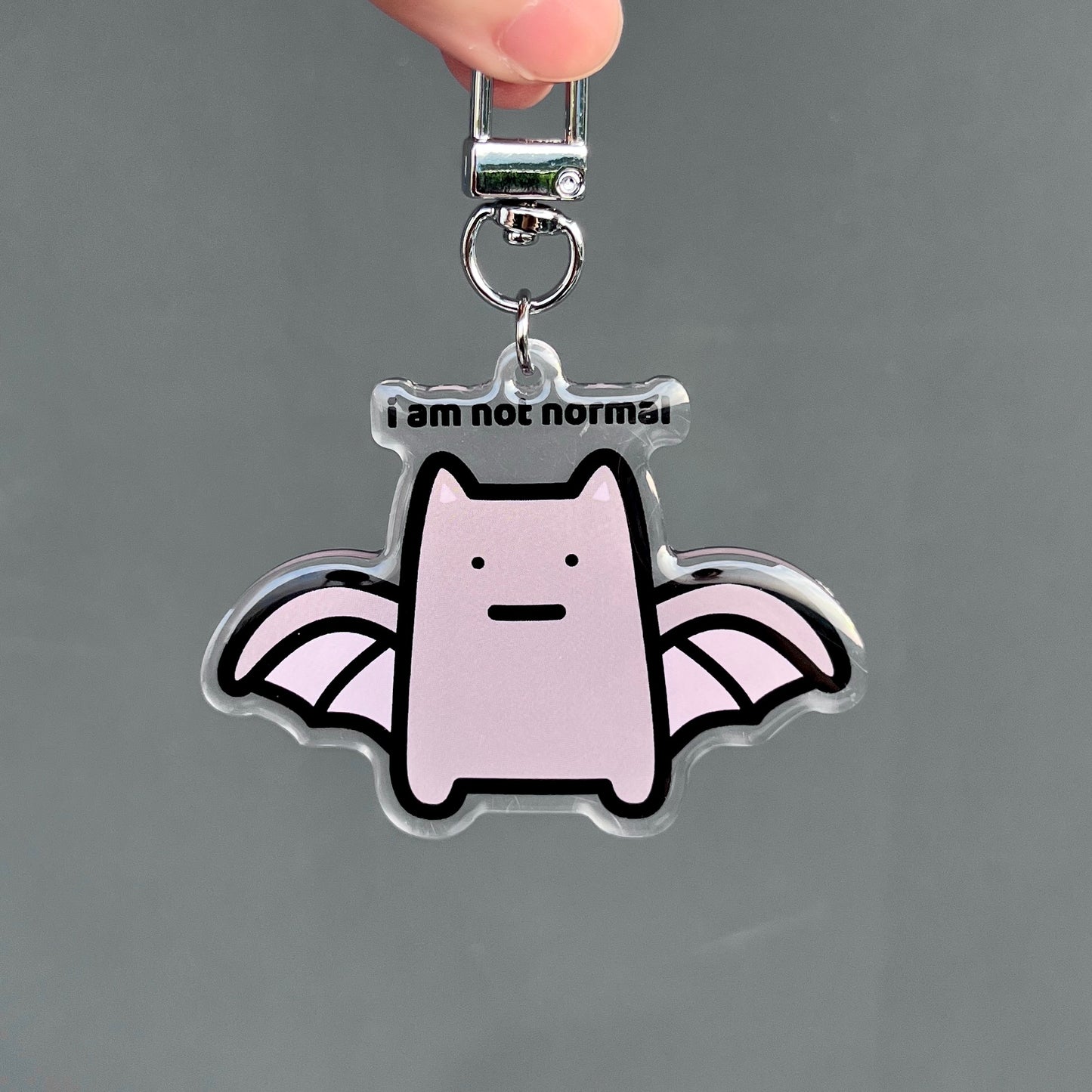 waterproof bat cat acrylic keychain with the text “I am not normal" on a plain background