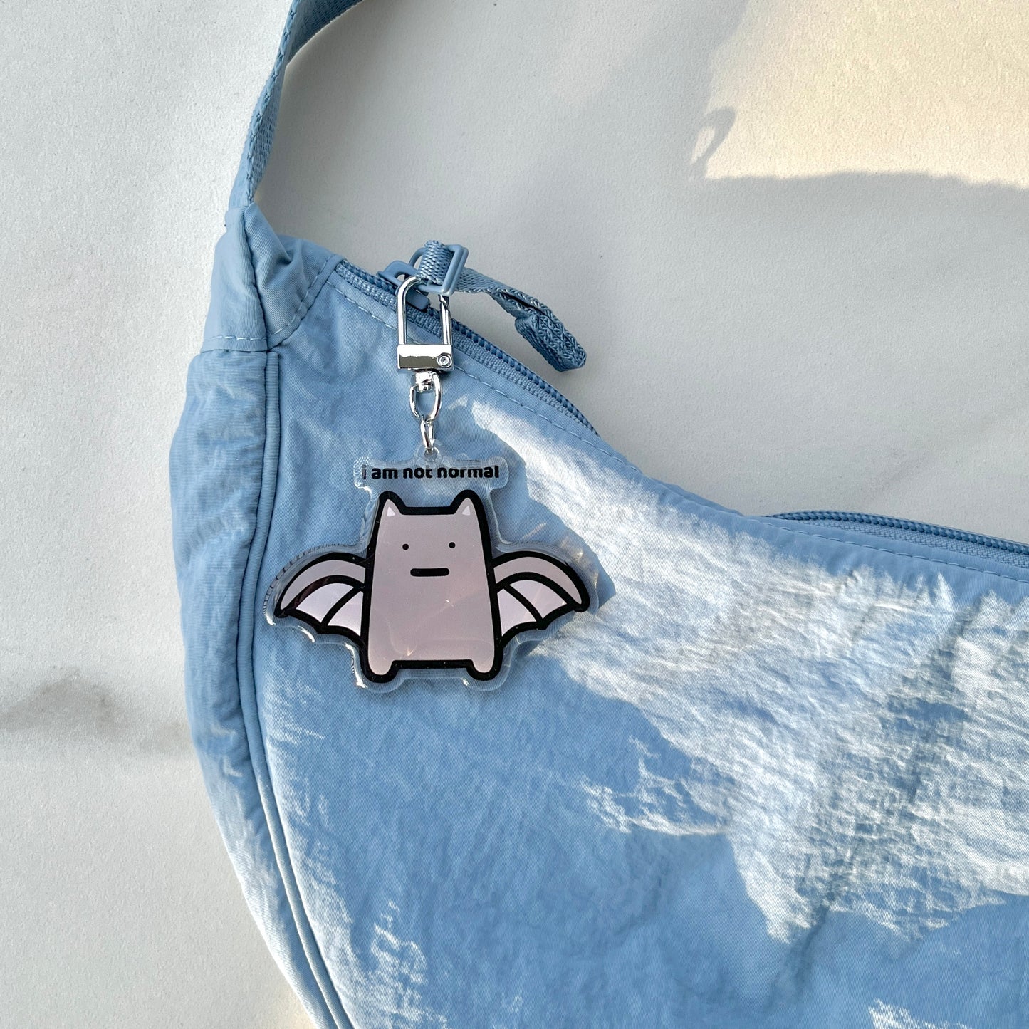 waterproof bat cat acrylic keychain with the text “I am not normal" on a bag