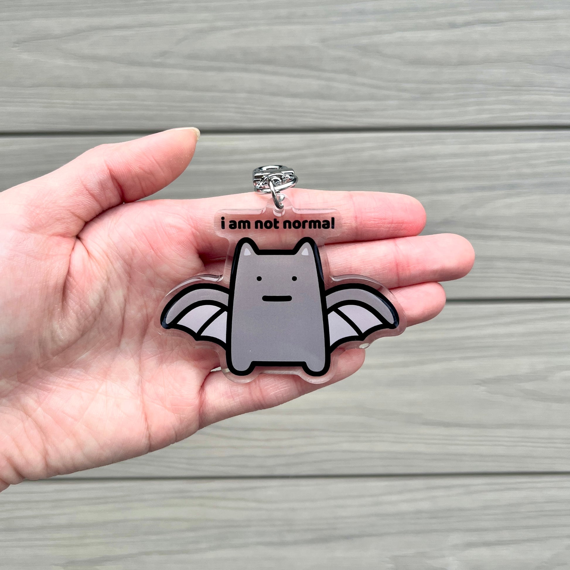 waterproof bat cat acrylic keychain with the text “I am not normal" on a person's hand