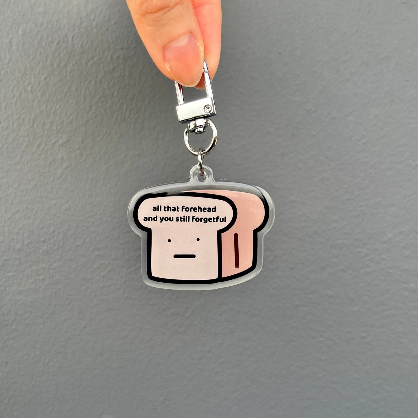 waterproof bread acrylic keychain with the text “All that forehead and you still forgetful" on a plain background