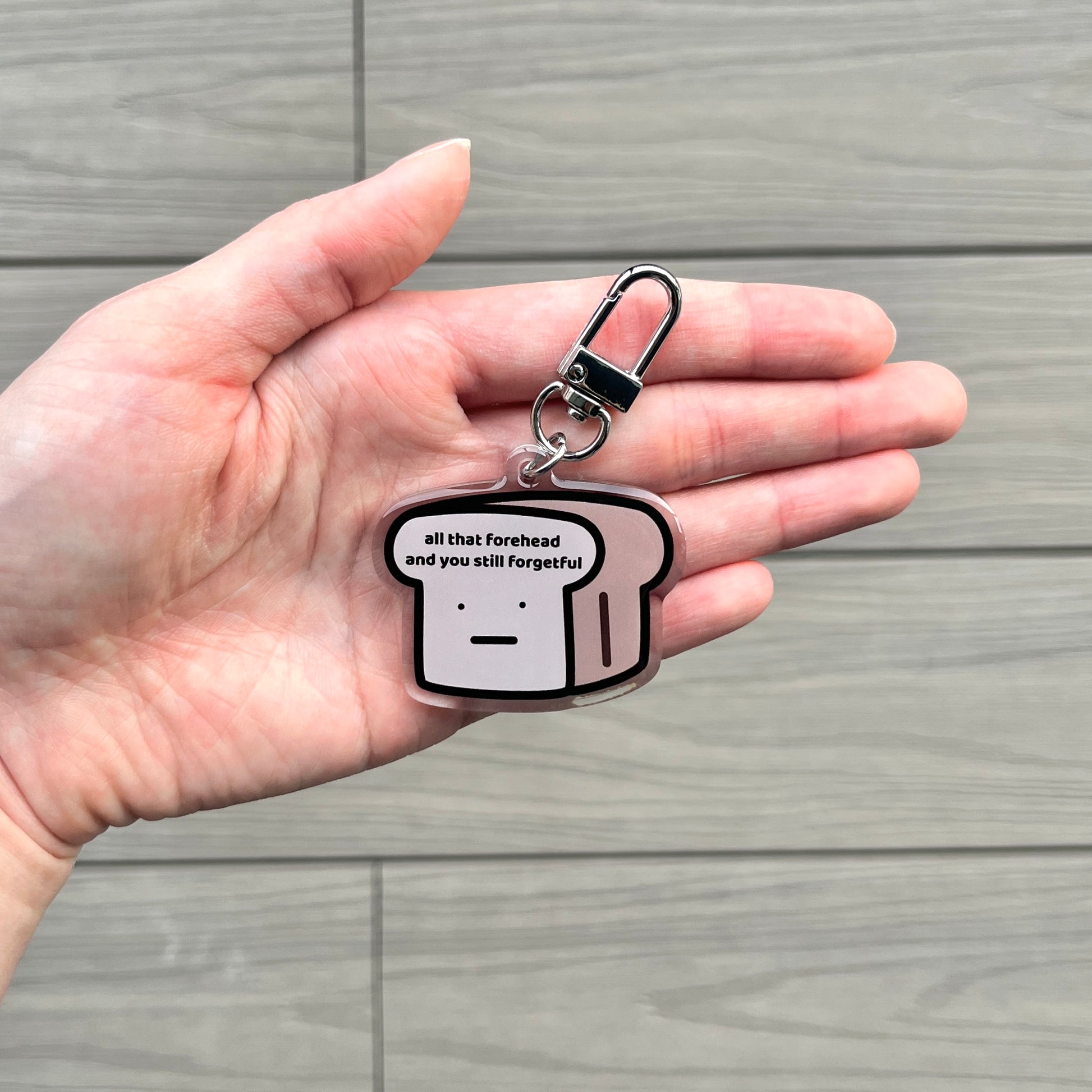 waterproof bread acrylic keychain with the text “All that forehead and you still forgetful" on a person's hand