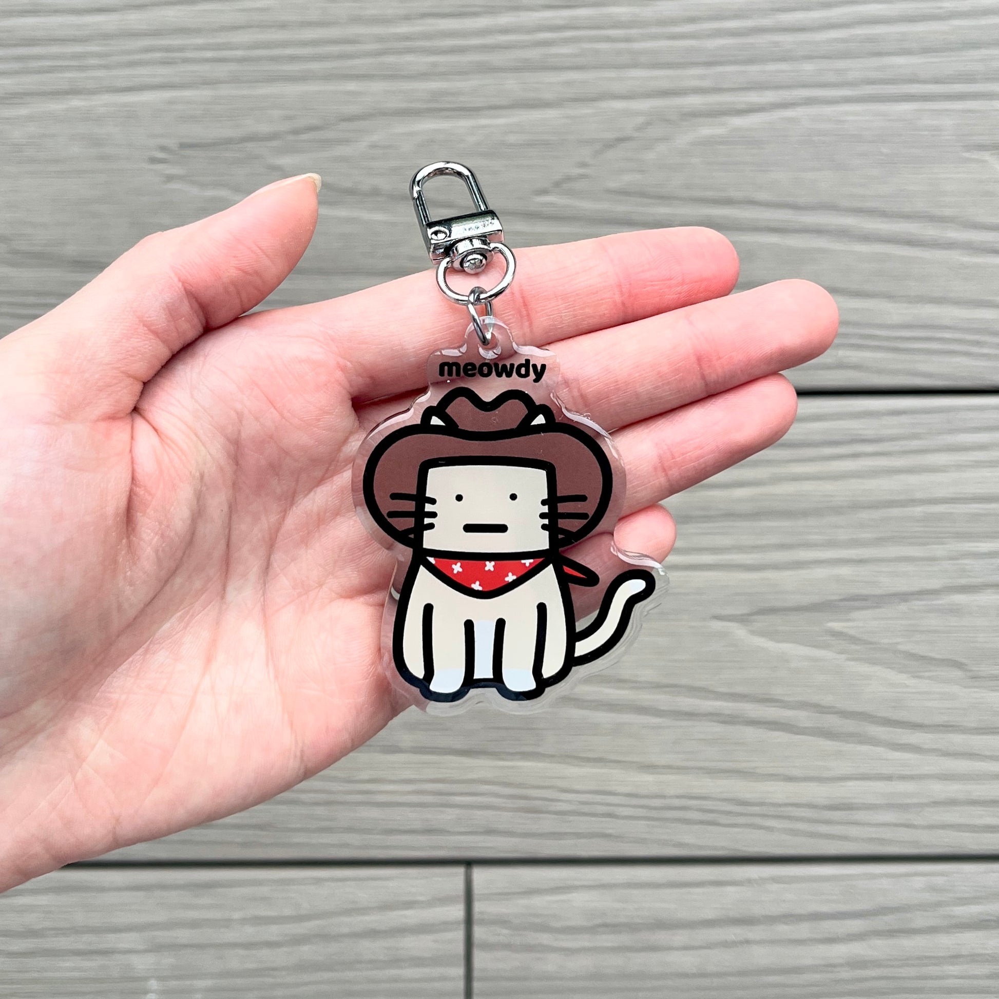 waterproof cat acrylic keychain with the text “Meowdy" on a person's hand