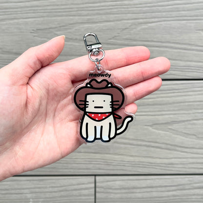 waterproof cat acrylic keychain with the text “Meowdy" on a person's hand