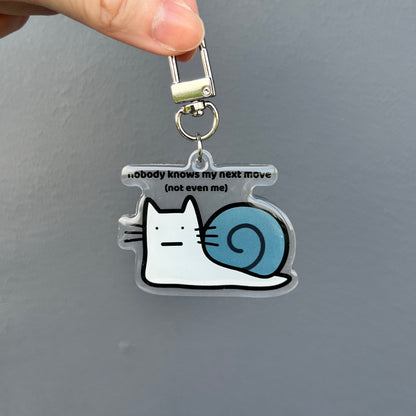 waterproof cat snail acrylic keychain with the text “Nobody knows my next move (Not even me)" on a plain background
