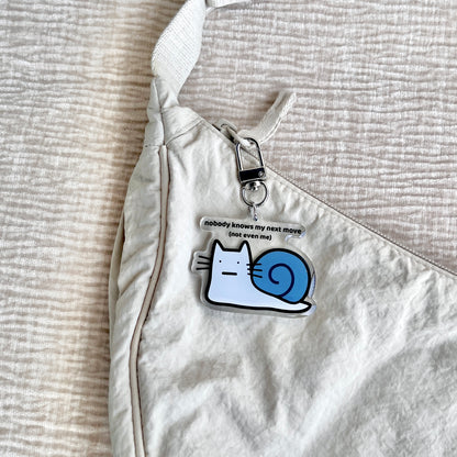 waterproof cat snail acrylic keychain with the text “Nobody knows my next move (Not even me)" on a bag