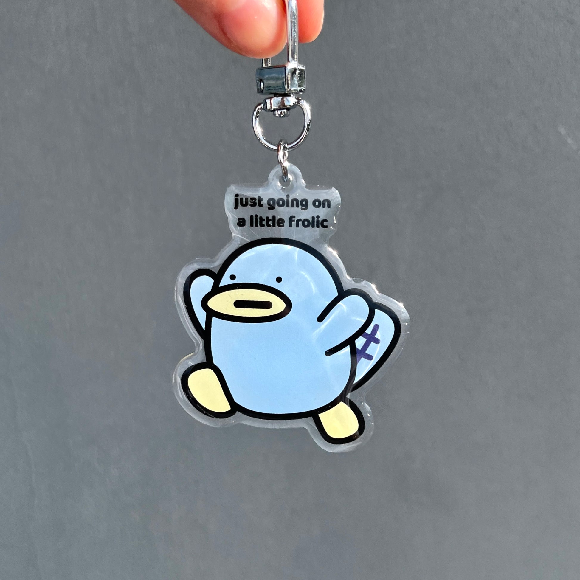 waterproof platypus acrylic keychain with the text “Just going on a little frolic" on a plain background