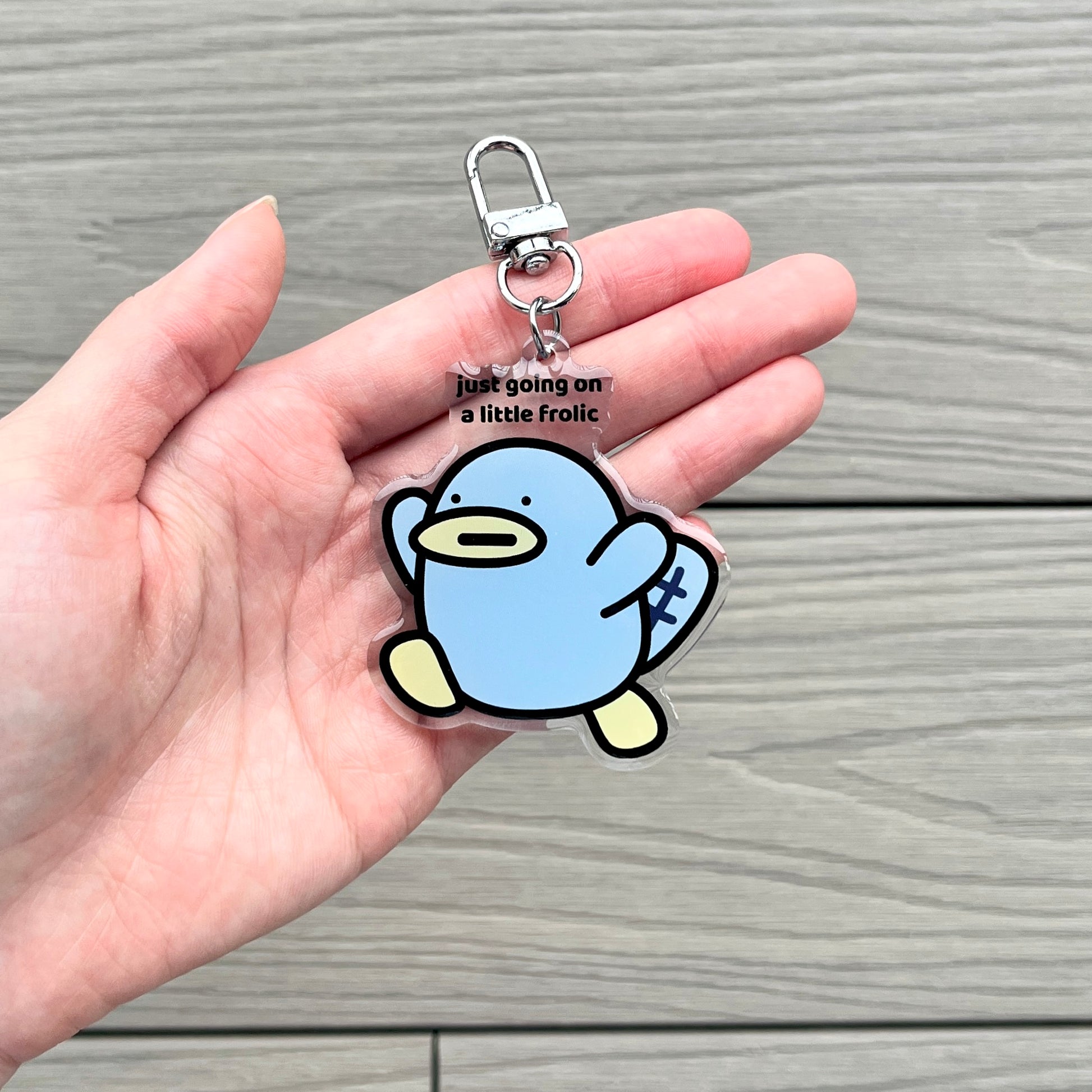 waterproof platypus acrylic keychain with the text “Just going on a little frolic" on a person's hand