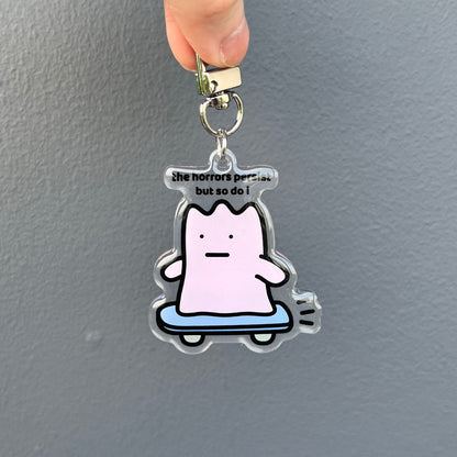 waterproof skateboard acrylic keychain with the text “The horrors persist but so do I" on a plain background