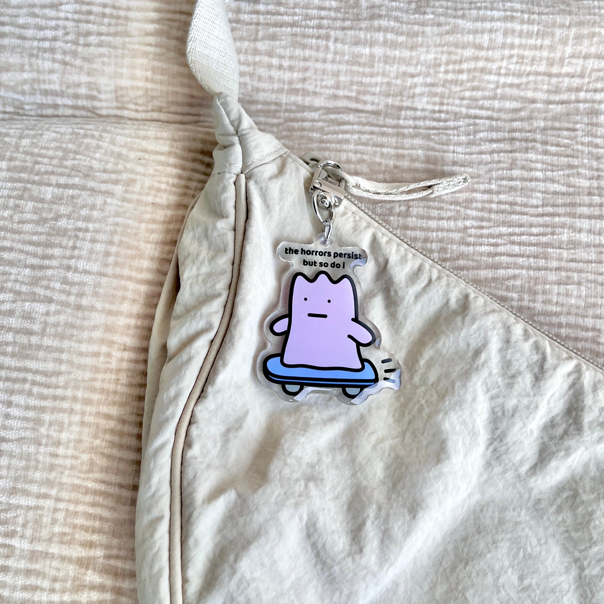 waterproof skateboard acrylic keychain with the text “The horrors persist but so do I" on a bag