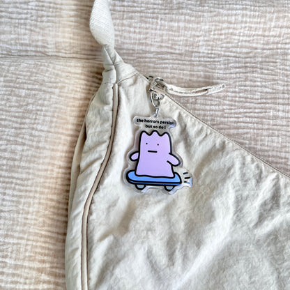 waterproof skateboard acrylic keychain with the text “The horrors persist but so do I" on a bag
